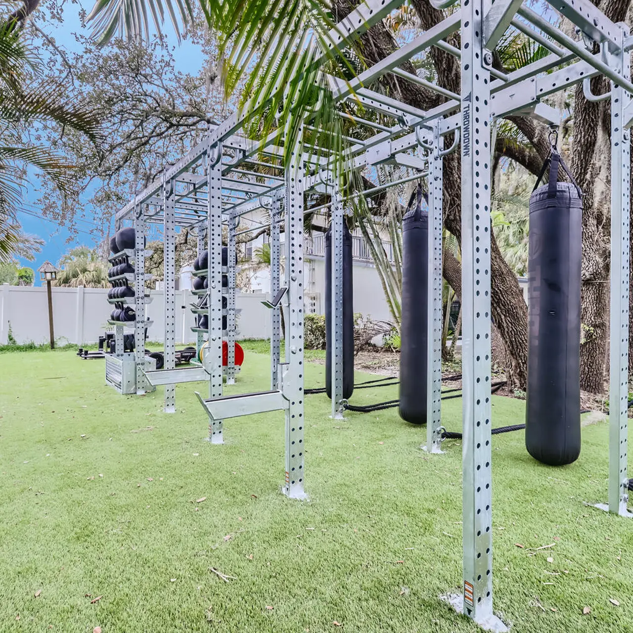 Outside fitness center with  punching bags, ropes and free weights surrounded by tree's and lawn
