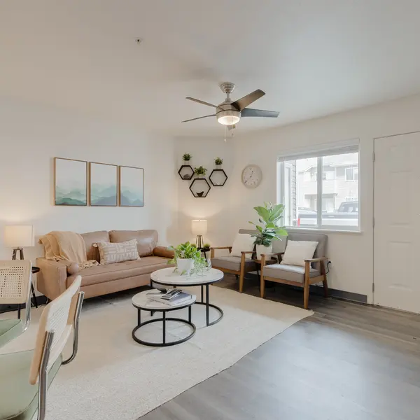 Modern apartment living room at The Landing at Clearwater in Moscow, Idaho, featuring a leather sofa, accent chairs, stylish decor, geometric wall shelves, framed artwork, and indoor plants. Bright natural lighting and warm tones create a cozy and inviting atmosphere.