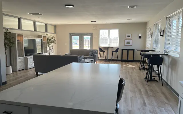 Modern living room with kitchen island, bar stools, couch, TV, and windows with blinds.