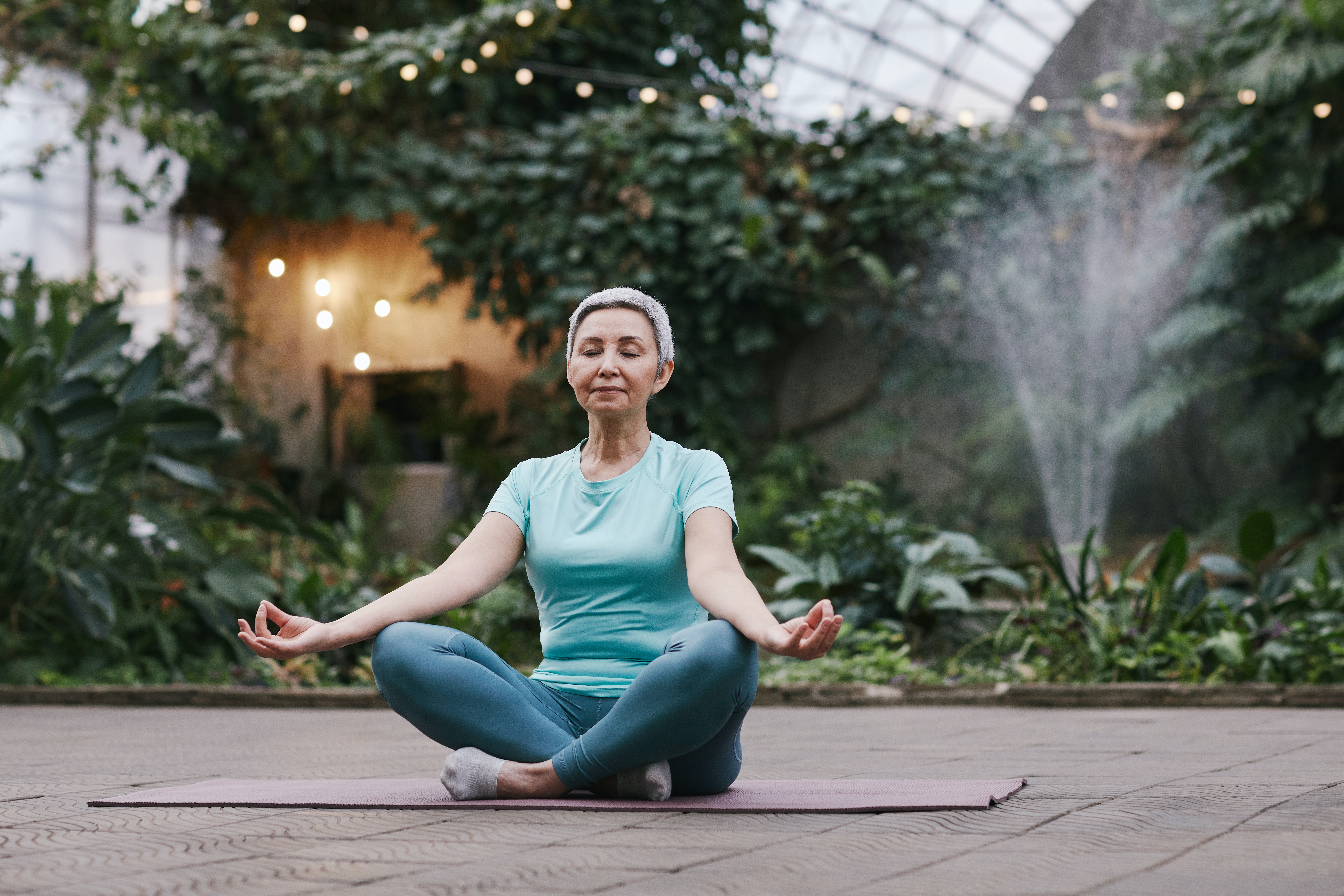 A woman practicing meditation in a serene greenhouse, surrounded by lush greenery and soft lighting.
