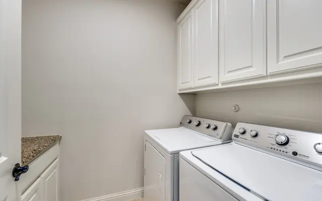 Modern Laundry Room A modern laundry room featuring a stacked washer and dryer, white cabinetry above and a granite countertop on the left side.