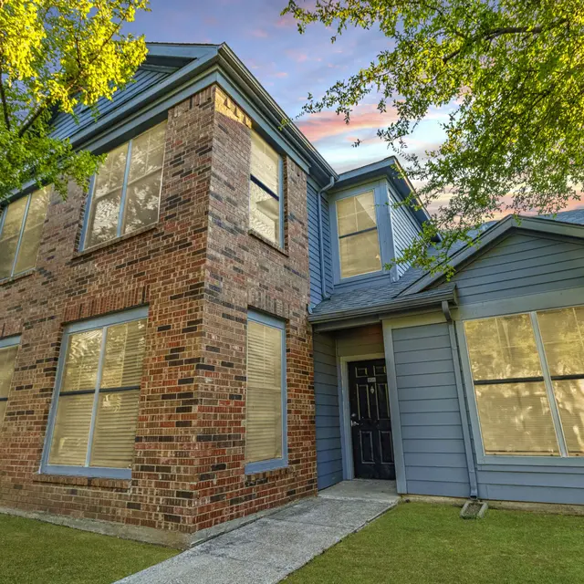 Exterior view of a two-story brick-framed house with multiple windows and a tree in the front yard.