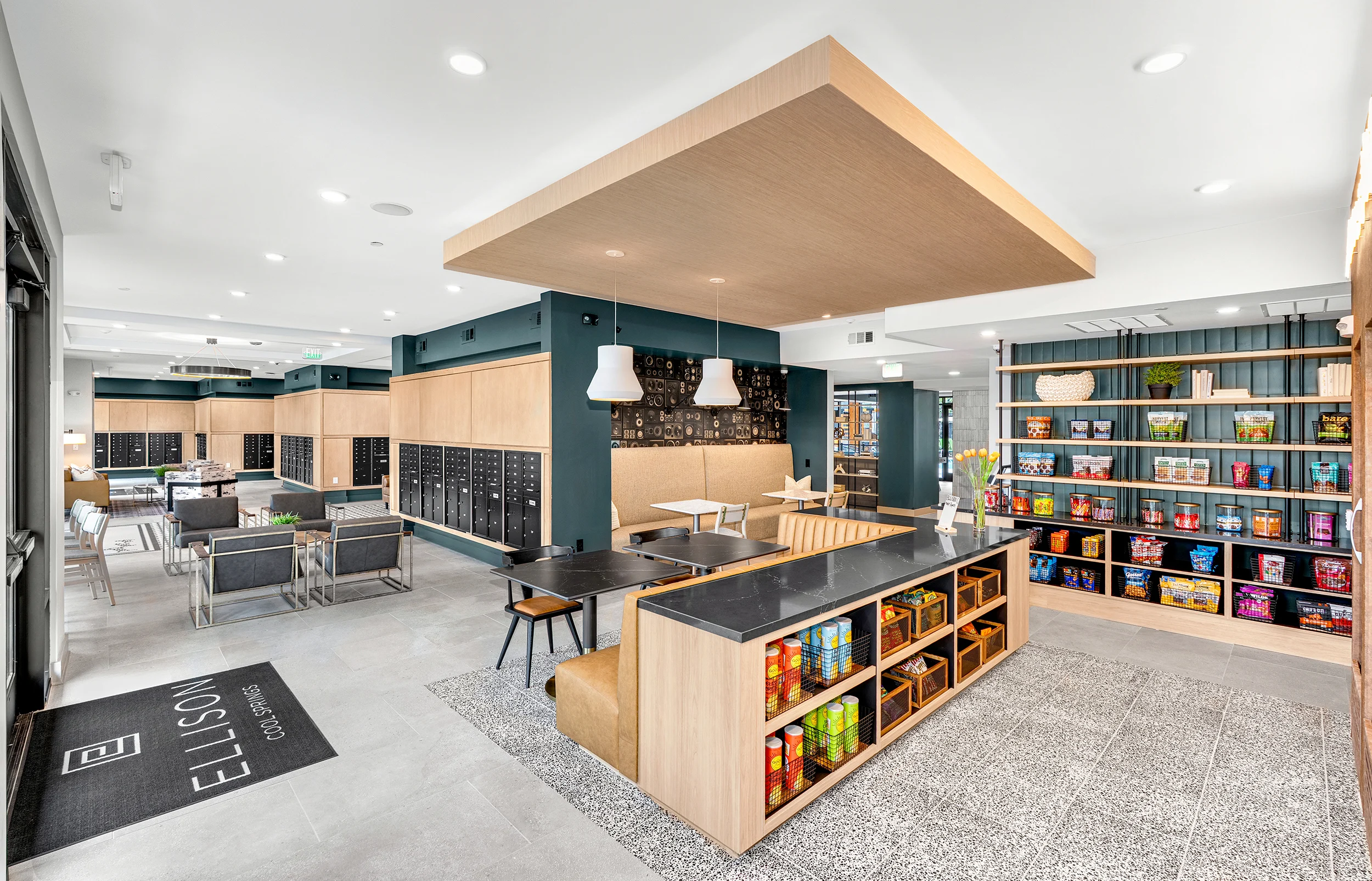 Stylish Community Lounge Brightly lit community space with modern decor, including seating areas, a display of various food and drink items, and lockers.