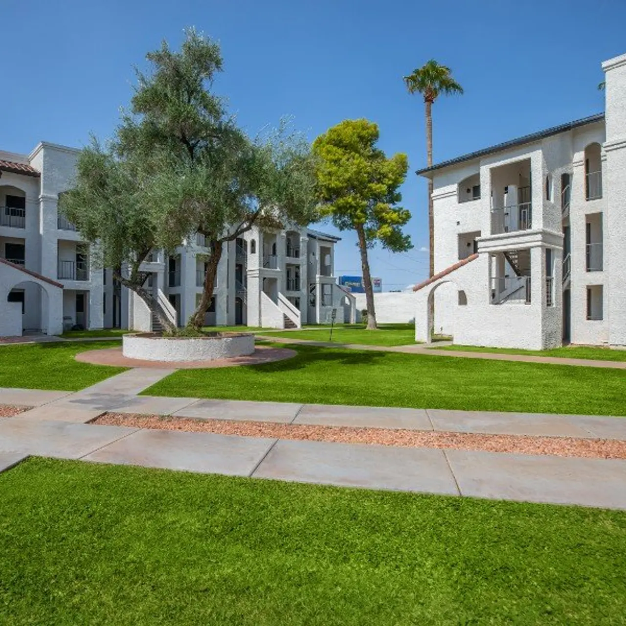 View of an apartment complex with white buildings, green lawns, and a clear blue sky.