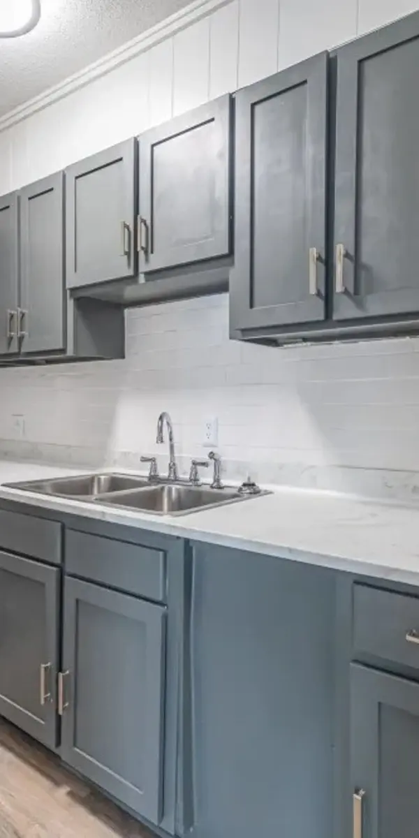 A modern kitchen with dark gray cabinets and black appliances, featuring a double sink and marble-like countertop.