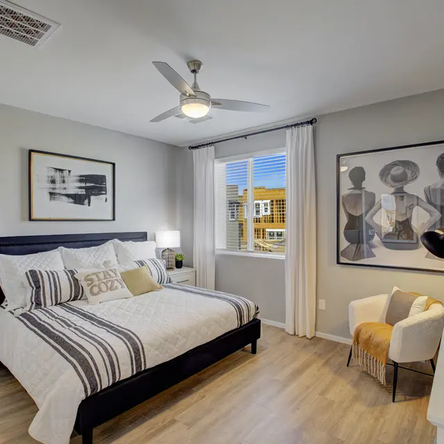 Modern bedroom featuring a queen bed with gray bedding, artwork on the walls, large window, and stylish decor.