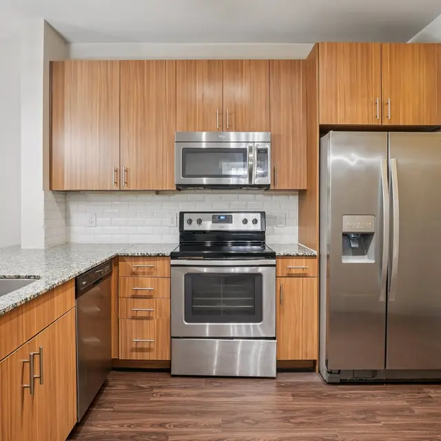 A modern kitchen featuring wooden cabinets, stainless steel appliances, and a large granite countertop.