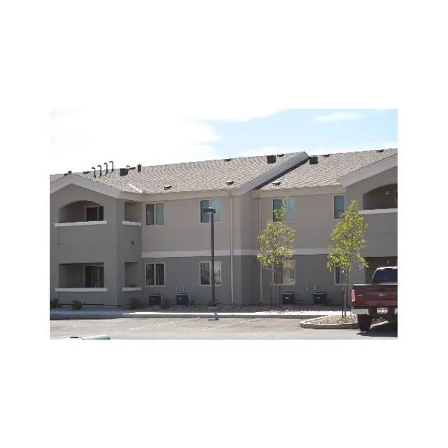 A light-colored apartment building with several windows and a roof. There are small trees nearby and a truck parked in front.