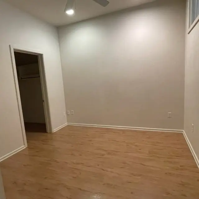 An empty room with wooden flooring, white walls, and a ceiling fan. There is a doorway leading to a closet on the left side of the image.