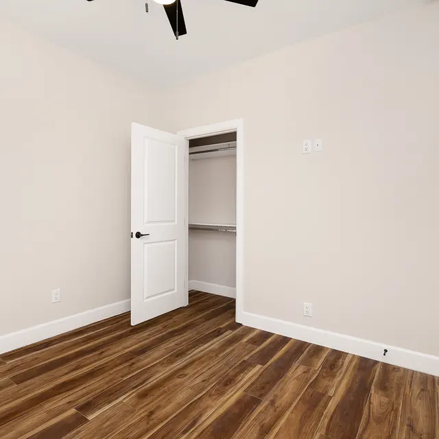 An empty room with light brown walls, wooden flooring, and an open door leading to a closet.