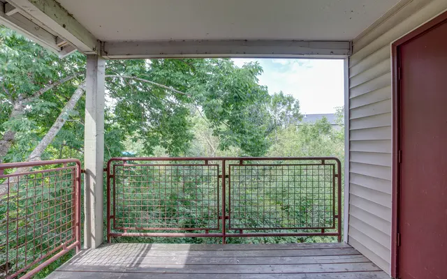 A wooden balcony with a metal railing overlooking lush greenery and trees
