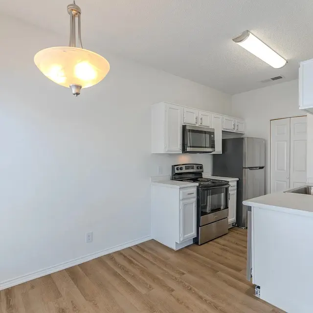 A bright and modern kitchen featuring white cabinetry, stainless steel appliances, and a spacious layout with wooden flooring.