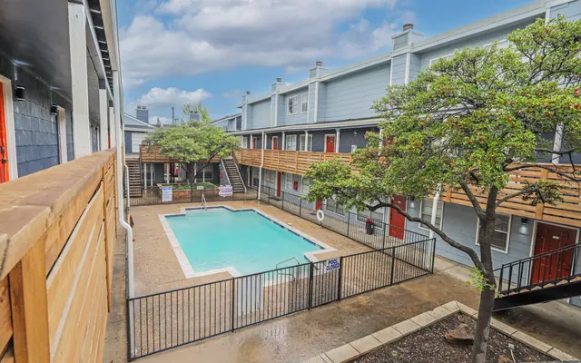 View of an apartment complex courtyard featuring a swimming pool surrounded by greenery and buildings.