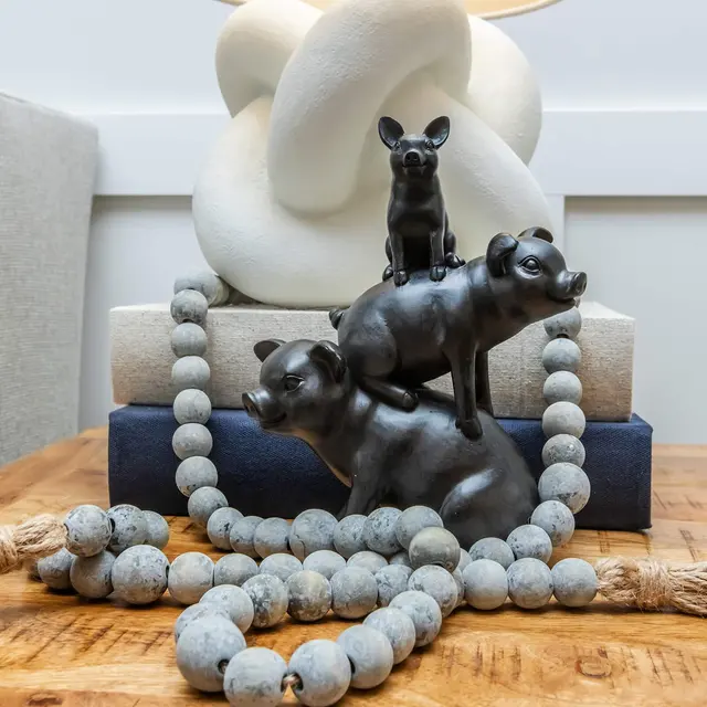 Charming Tabletop Decor A tabletop arrangement featuring decorative black figurines of a pig and a small dog, stacked artistically. There are also wooden beads and books displayed beneath a soft light source.