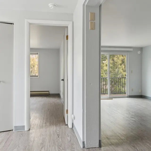 Modern Apartment Interior A view of a modern apartment interior showcasing an open layout, featuring a door frame leading to another room, sliding glass doors that open to a balcony, and a light-colored flooring.