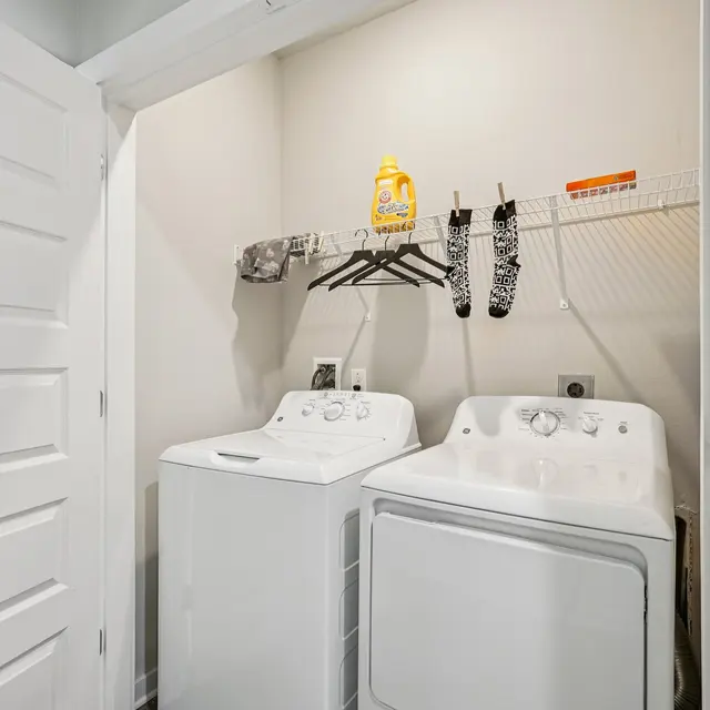 Laundry Room Setup A laundry room with a washer and dryer side by side, hanging socks and a bottle of detergent on a shelf above.