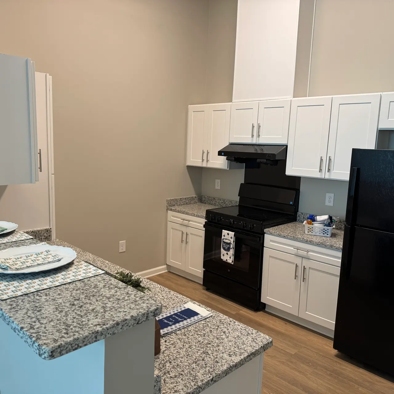 A modern kitchen featuring white cabinetry, granite countertops, and black appliances.