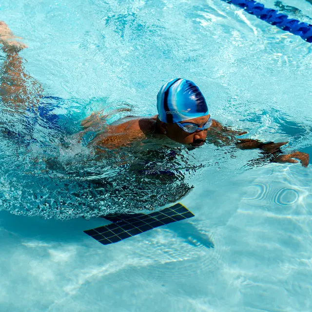 A swimmer wearing a blue swim cap and goggles gliding through clear water in a swimming pool, with a focus on the swimmer's upper body in motion.