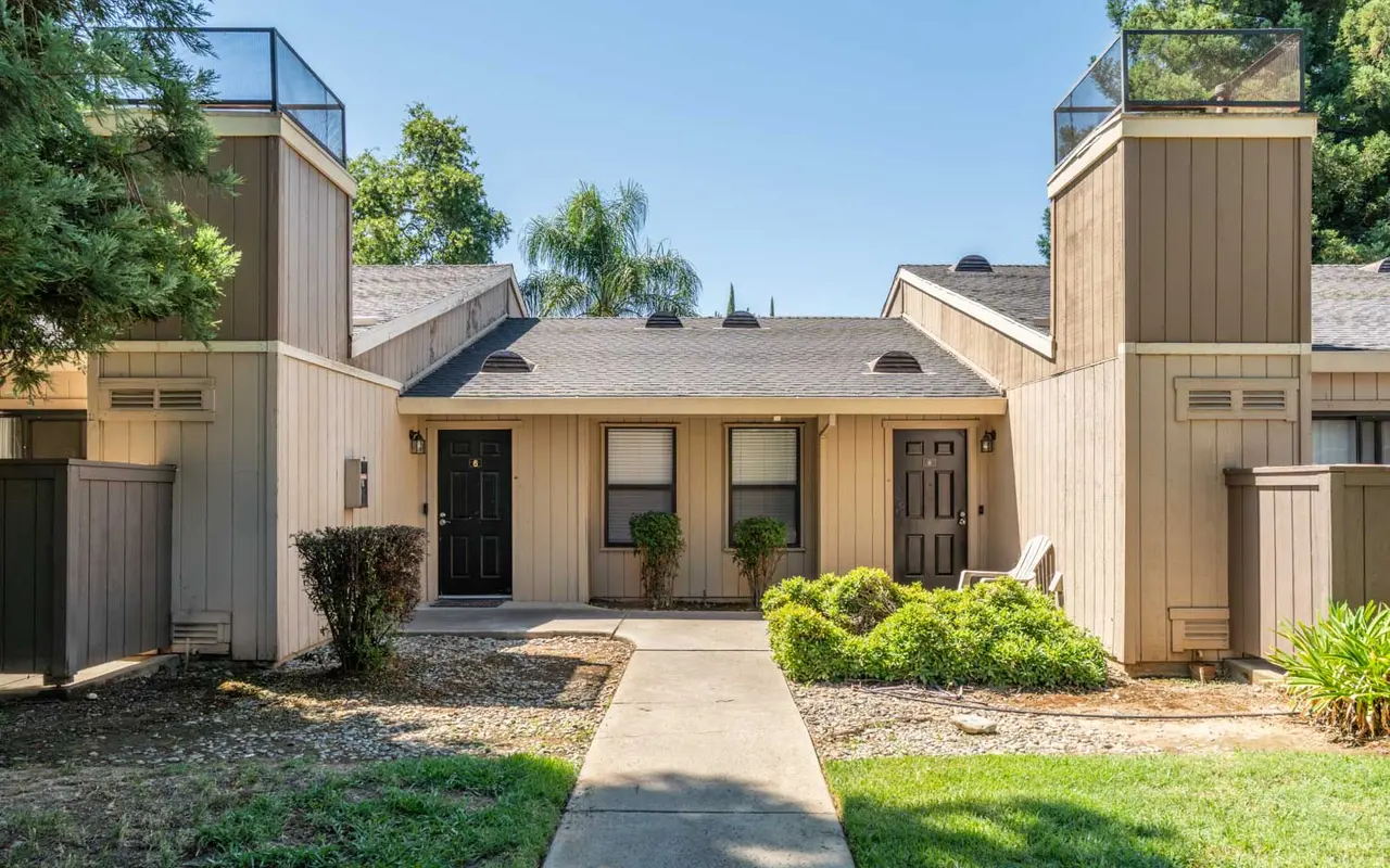 Front view of an apartment complex with two doors, greenery, and blue sky.