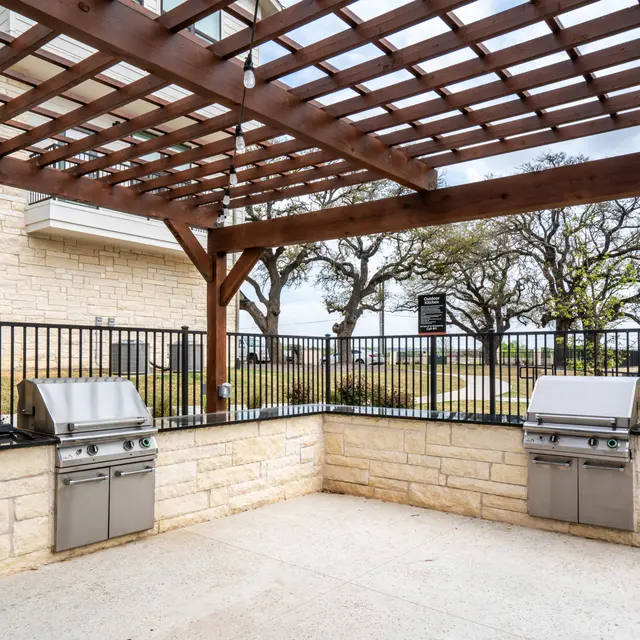 Outdoor grilling area with two stainless steel grills under a wooden pergola