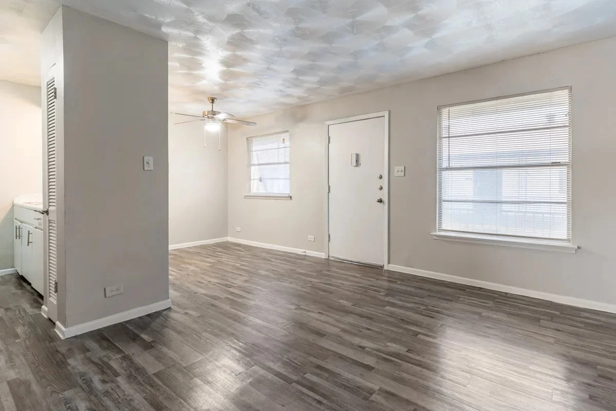 Modern Living Room Interior Empty living room with gray wooden flooring, white walls, a ceiling fan, and windows.