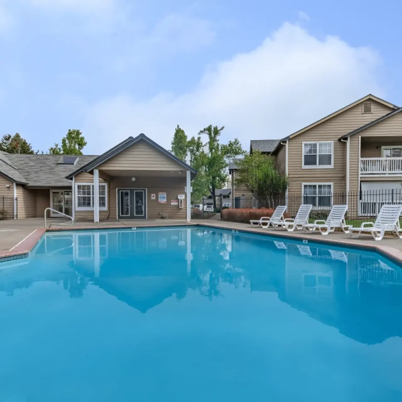 A clear swimming pool surrounded by lounge chairs, with residential buildings in the background.