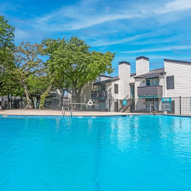 A clear blue swimming pool surrounded by trees and residential buildings.