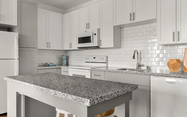 kitchen area with a granite countertop, bar stools, an all-white appliances and cabinets at apartment in Ewa Beach, HI - Room, Indoors, Kitchen