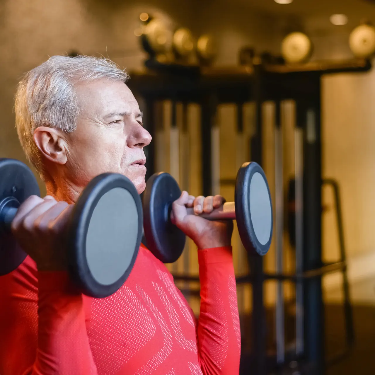 Older man exercising with dumbbells in a gym setting