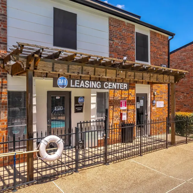 Exterior view of a leasing center at an apartment complex featuring brick architecture and a wooden pergola.