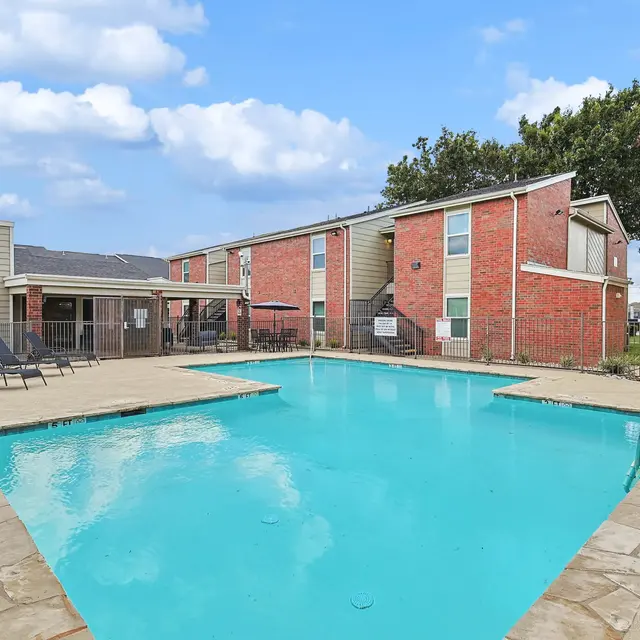 Swimming pool area of an apartment complex with lounge chairs and surrounded by buildings.