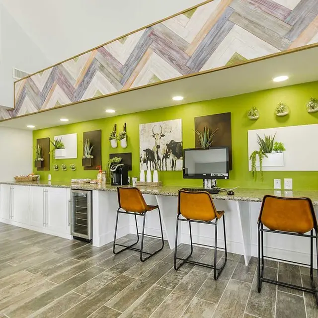Coffee bar and three tall bar stools with a computer against a lime green statement wall in the resident lounge at Edge Studios