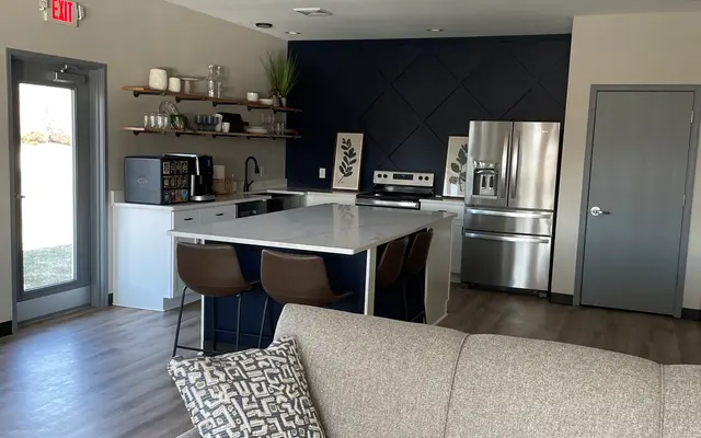 Modern living room with a beige sofa, kitchen with stainless steel appliances, and geometric backsplash design.