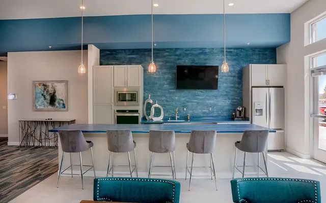 Modern kitchen with bar stools, blue backsplash, pendant lights, and stainless steel appliances.