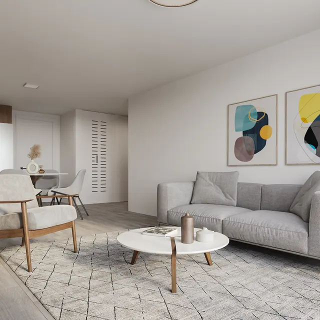 A modern living room featuring a gray sofa and a wooden chair. A round coffee table sits on a textured rug. Two colorful abstract paintings are on the wall, and there is a dining area in the background with a table and chairs.