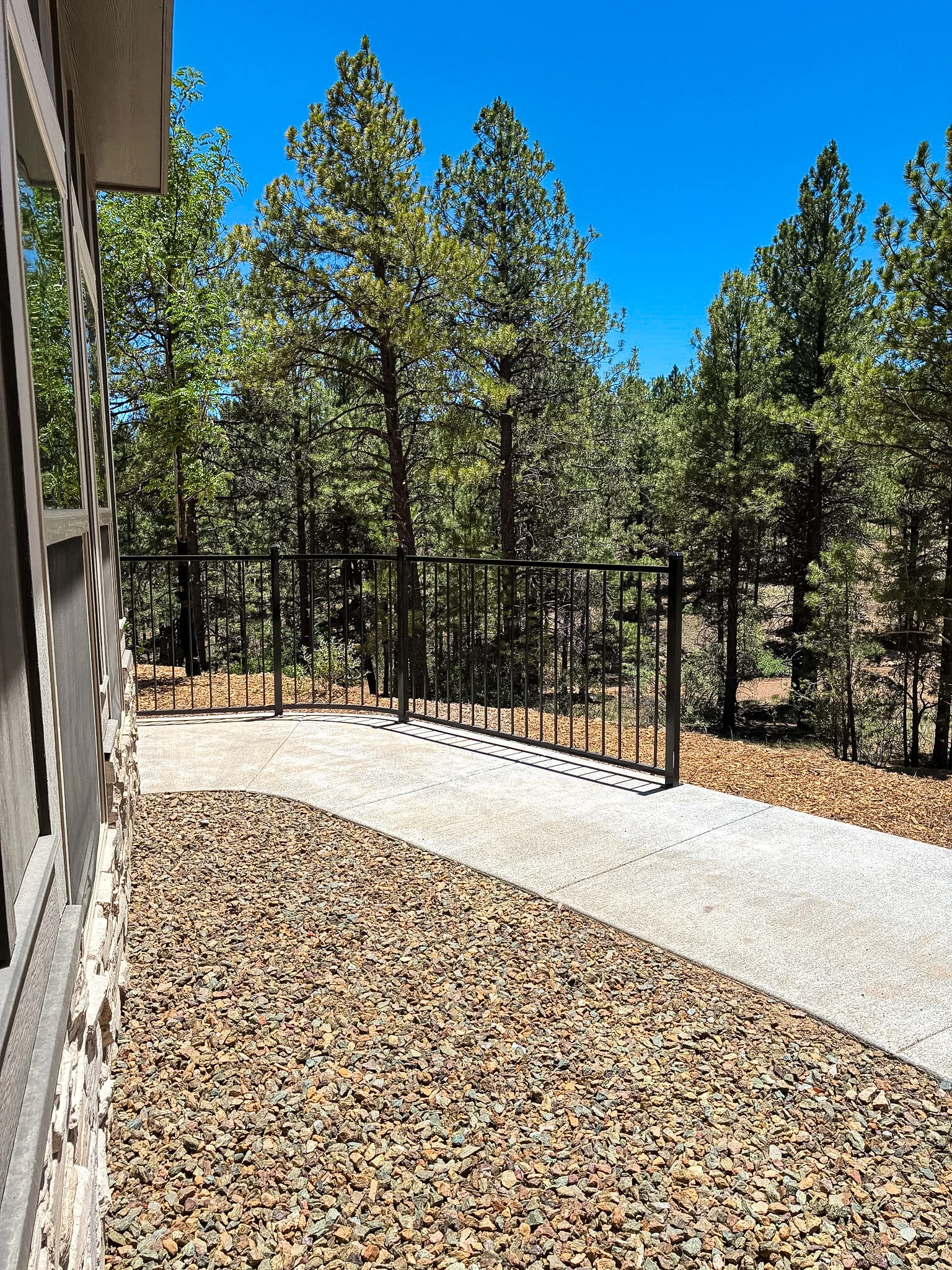 A patio area with a railing overlooking a forest of tall trees under a clear blue sky.