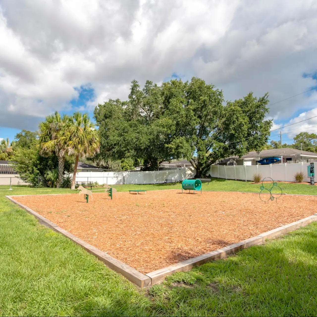 Dog park area of our community fitted with a play box, agility equipment, and a freshly cut garden