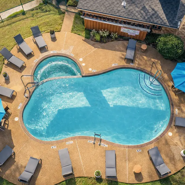 Aerial view of a swimming pool area featuring a blue pool and a hot tub, surrounded by lounge chairs and umbrellas.