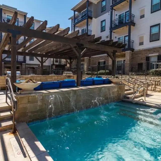 A beautiful outdoor pool area with a pergola and seating, surrounded by modern apartment buildings.