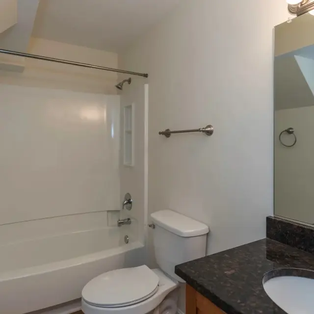 A clean and modern bathroom featuring a shower-tub combo, toilet, and sink with a mirror above it.