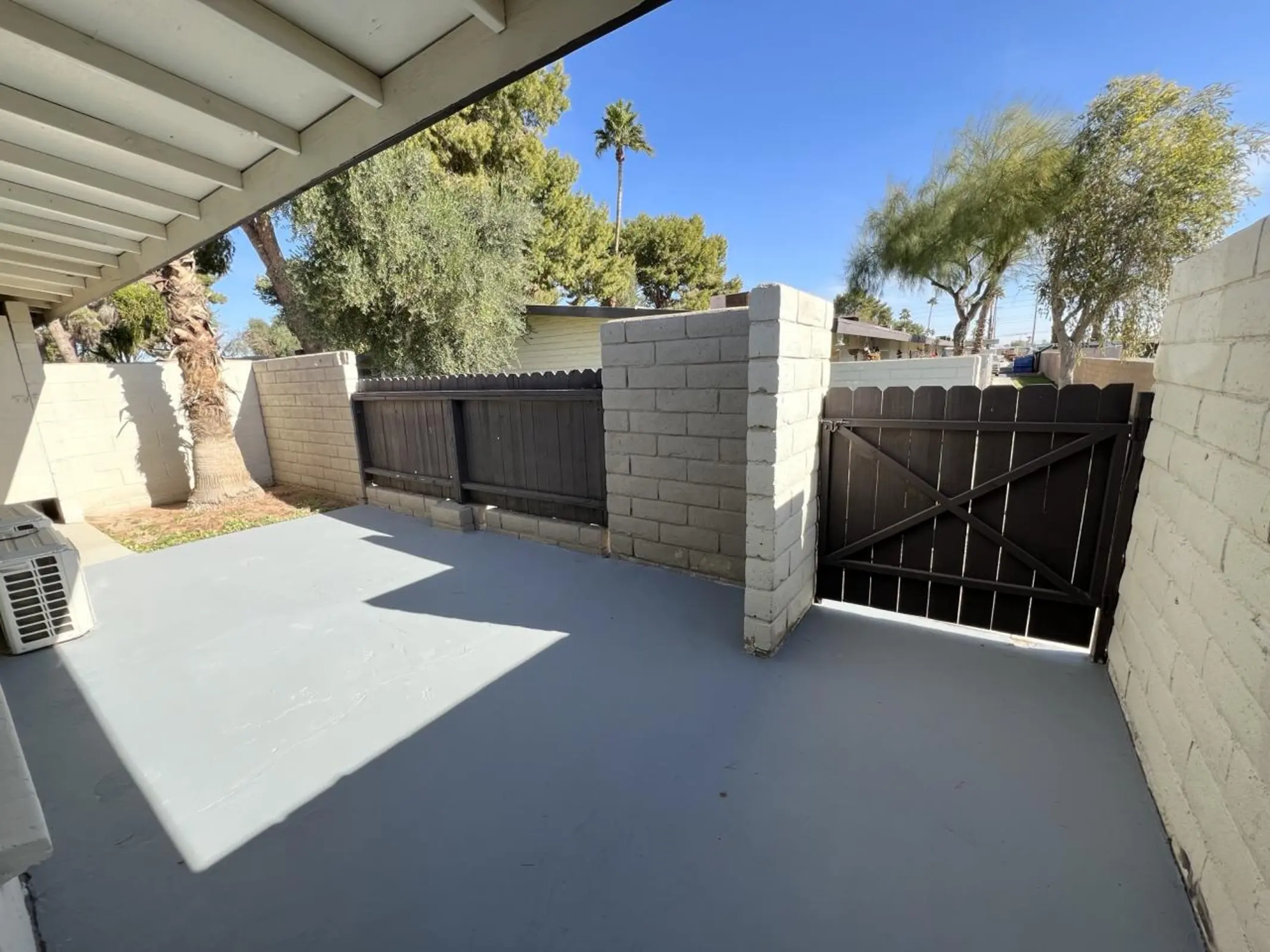 Patio and fenced yard with a wooden gate and trees beyond.