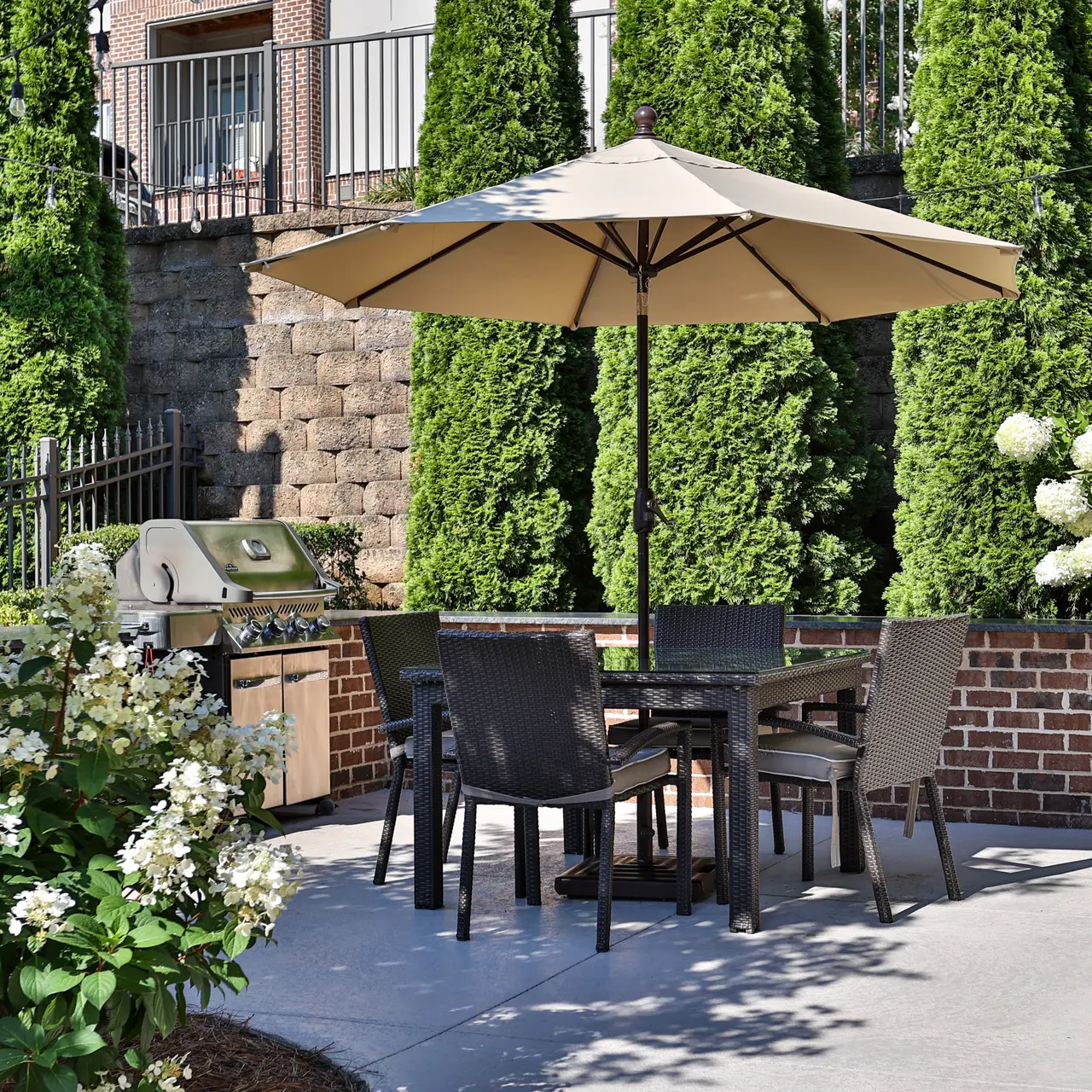 Charming Outdoor Patio Space An outdoor patio area featuring a table with chairs under a large umbrella, surrounded by greenery and flowering plants.