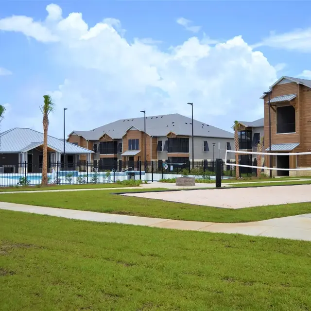 View of an apartment complex featuring a volleyball court and swimming pool in the background.