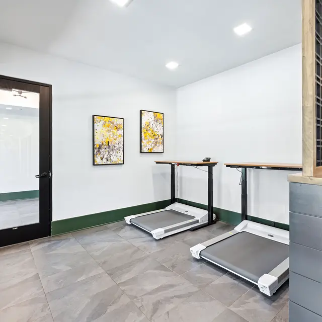 A modern fitness room featuring two treadmills, artwork on the wall, and a door leading to another space.