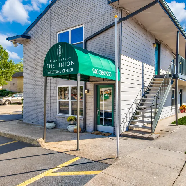 An exterior view of the Missouri The Union Welcome Center showing a green awning entrance, concrete pathway, stairs, and nearby parking.