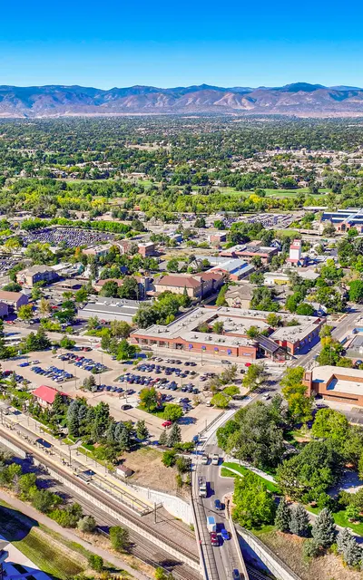 Aerial view of a town with green parks, urban areas, and mountains in the background.