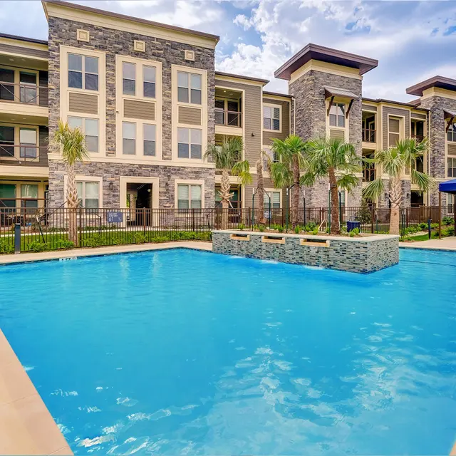 A modern apartment complex with a swimming pool surrounded by lounge chairs and palm trees.