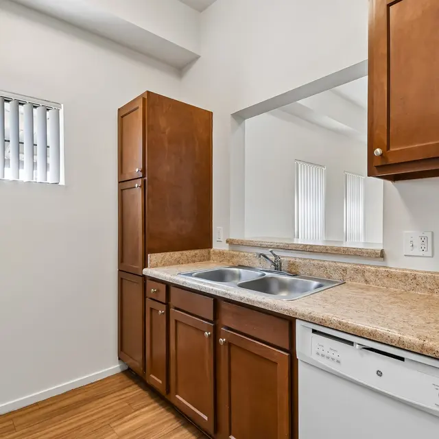 Modern Kitchen Interior An interior view of a modern kitchen featuring wooden cabinets, a sink, and a dishwasher. White walls and a window with vertical blinds allow natural light to enter the space.