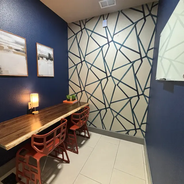 A small, modern meeting space with a long wooden table surrounded by red chairs, blue walls, and patterned accent wall.