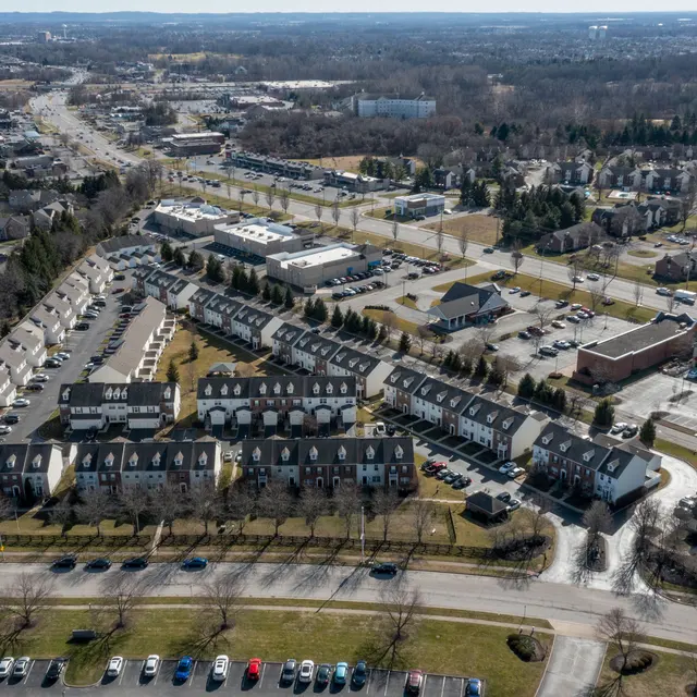 Aerial view of a suburban neighborhood with townhouses, parking lots, and nearby commercial areas.